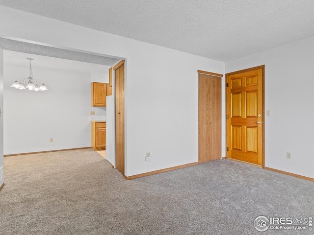 carpeted spare room featuring a textured ceiling and a notable chandelier