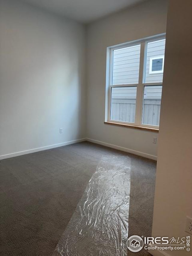 spare room featuring baseboards and dark colored carpet