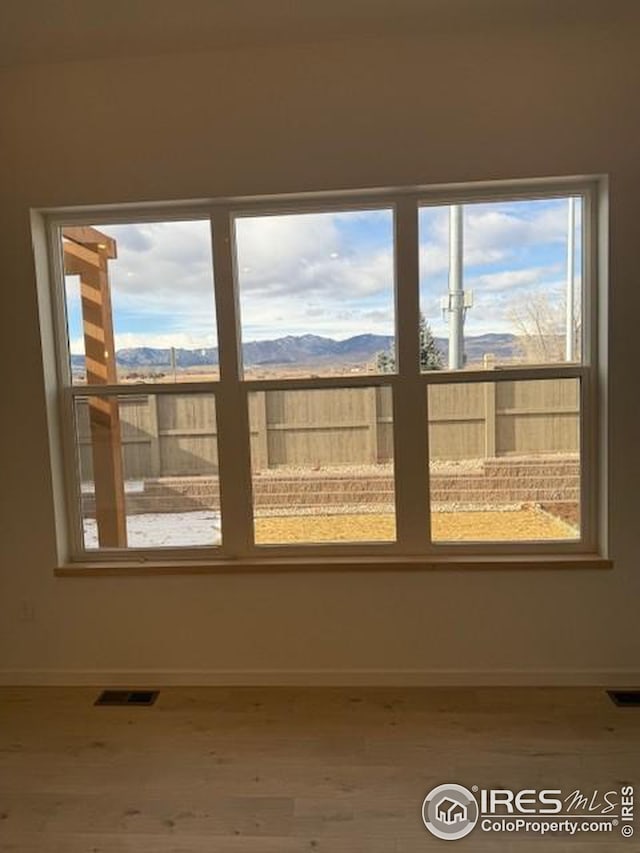 empty room with visible vents, a mountain view, baseboards, and wood finished floors