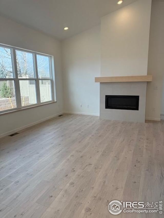 unfurnished living room with recessed lighting, wood finished floors, visible vents, baseboards, and a glass covered fireplace