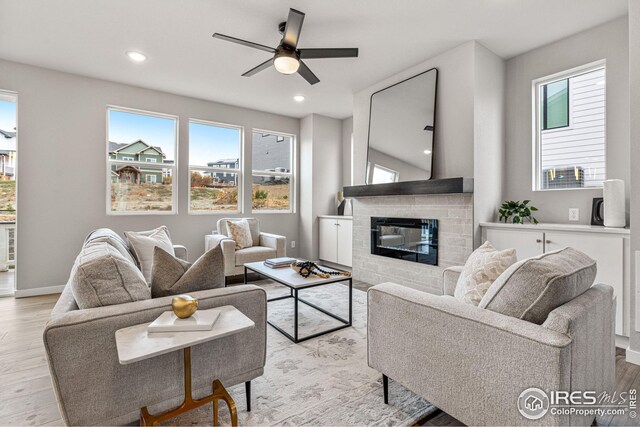 living room featuring light hardwood / wood-style floors, a brick fireplace, ceiling fan, and a wealth of natural light