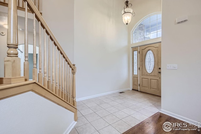 foyer entrance with a towering ceiling, light tile patterned floors, baseboards, and stairway