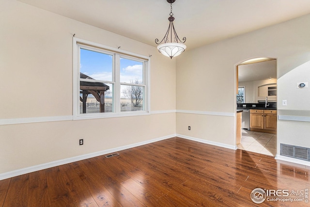 unfurnished dining area featuring hardwood / wood-style flooring, visible vents, arched walkways, and a sink