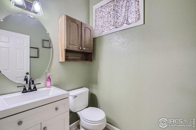 half bath with a textured wall, vanity, toilet, and baseboards