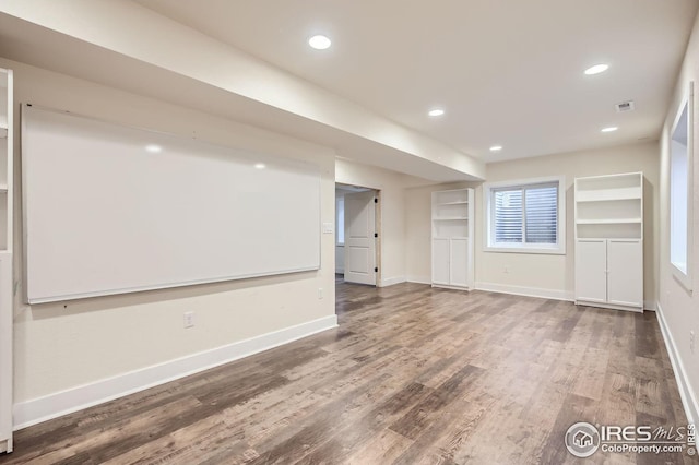 empty room with built in shelves, recessed lighting, baseboards, and wood finished floors