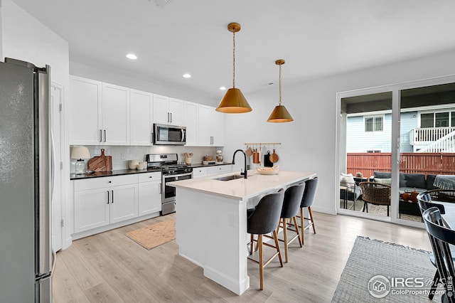 kitchen featuring white cabinets, sink, hanging light fixtures, light wood-type flooring, and stainless steel appliances