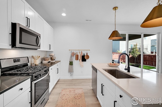 kitchen featuring pendant lighting, sink, light hardwood / wood-style floors, white cabinetry, and stainless steel appliances