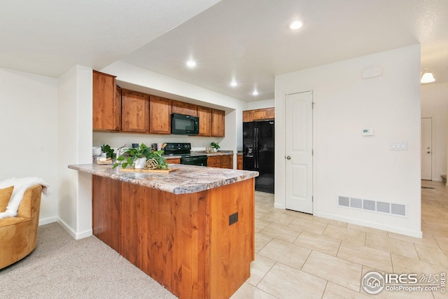 kitchen featuring a peninsula, black appliances, brown cabinets, and visible vents