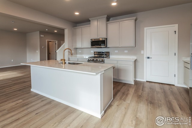 kitchen with light wood-type flooring, a kitchen island with sink, appliances with stainless steel finishes, and sink