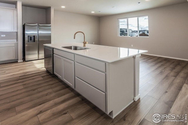 kitchen featuring dark wood-type flooring, sink, stainless steel appliances, and a center island with sink