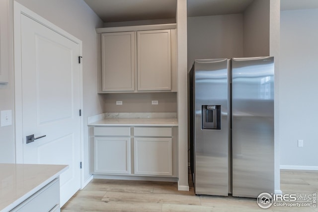 kitchen featuring light stone countertops, white cabinets, stainless steel fridge with ice dispenser, and light hardwood / wood-style flooring