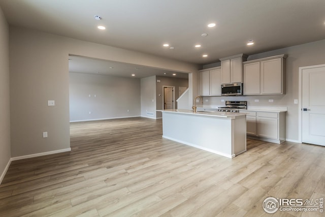 kitchen featuring stainless steel appliances, an island with sink, sink, gray cabinets, and light hardwood / wood-style flooring