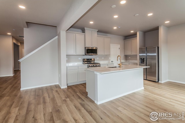 kitchen with light hardwood / wood-style flooring, sink, stainless steel appliances, and a center island with sink