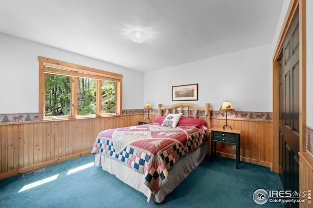 bedroom with visible vents, wooden walls, wainscoting, and dark colored carpet