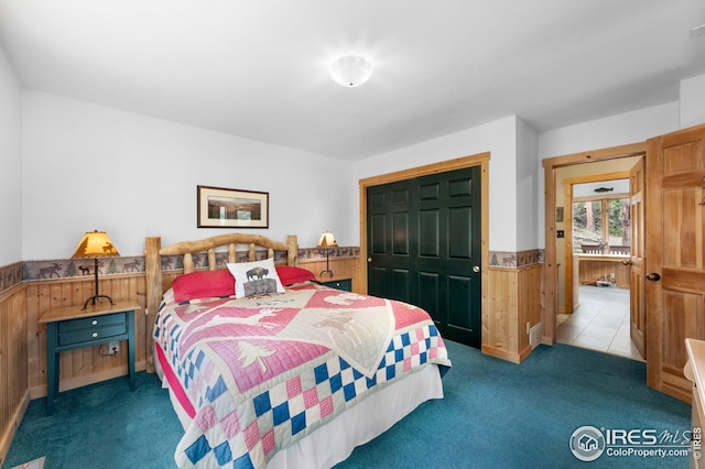 bedroom featuring a wainscoted wall, wooden walls, a closet, and carpet floors