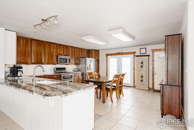 kitchen featuring stainless steel appliances, sink, light tile patterned flooring, kitchen peninsula, and light stone countertops