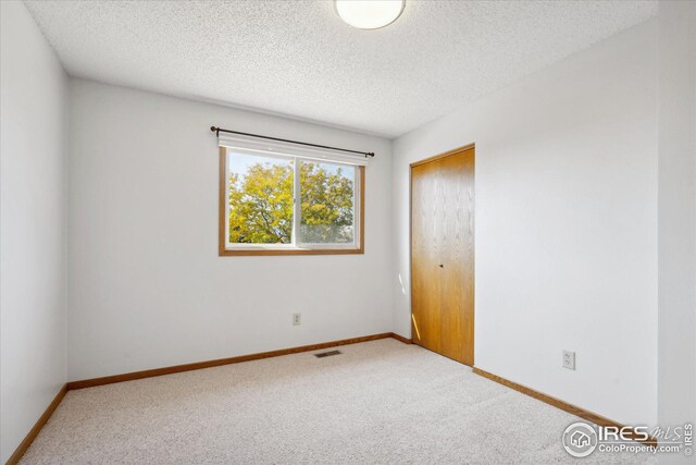 carpeted empty room with visible vents, a textured ceiling, and baseboards