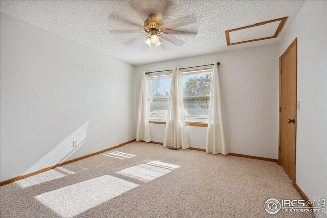 empty room featuring attic access, baseboards, a textured ceiling, and light colored carpet