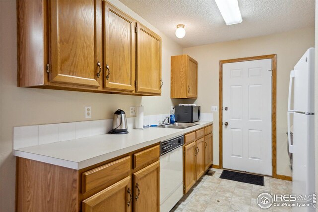 kitchen featuring brown cabinets, light countertops, a sink, a textured ceiling, and white appliances