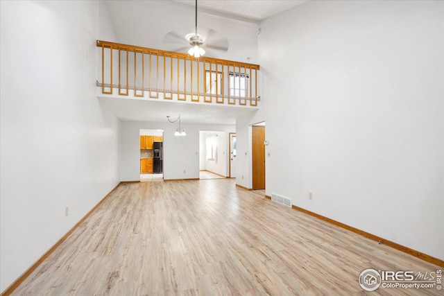 unfurnished living room with baseboards, a towering ceiling, visible vents, and light wood-style floors