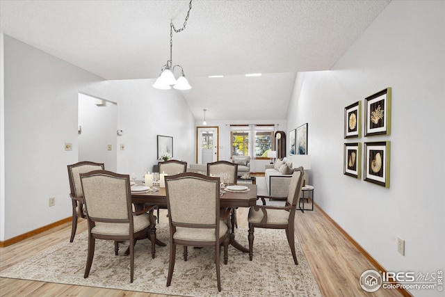 dining space with vaulted ceiling, a textured ceiling, light wood-type flooring, and a chandelier