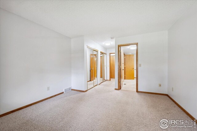 unfurnished bedroom featuring light carpet, baseboards, and a textured ceiling