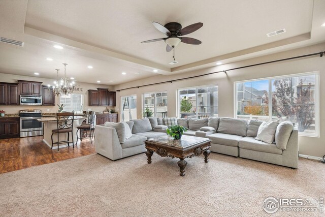 living room featuring ceiling fan with notable chandelier, a raised ceiling, and carpet flooring