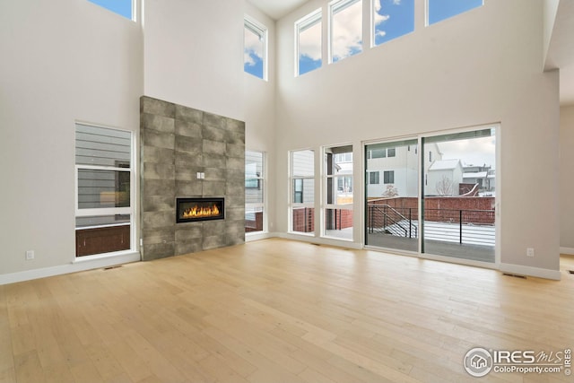 unfurnished living room with a towering ceiling, a tile fireplace, and light hardwood / wood-style flooring