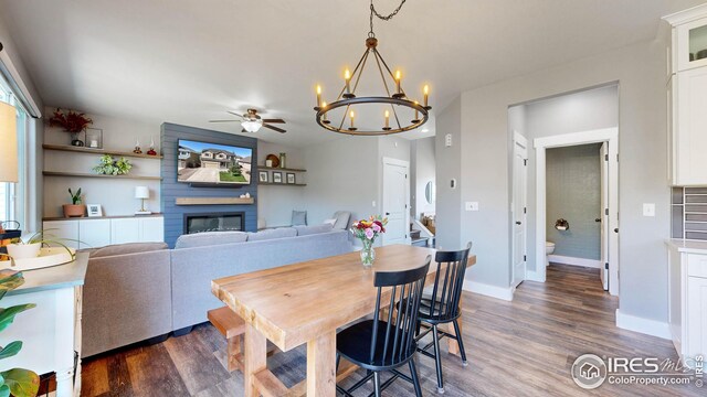 dining area featuring dark hardwood / wood-style flooring, a large fireplace, and ceiling fan with notable chandelier