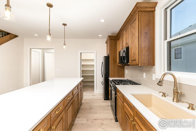 kitchen featuring tasteful backsplash, brown cabinets, light wood-type flooring, black appliances, and a sink