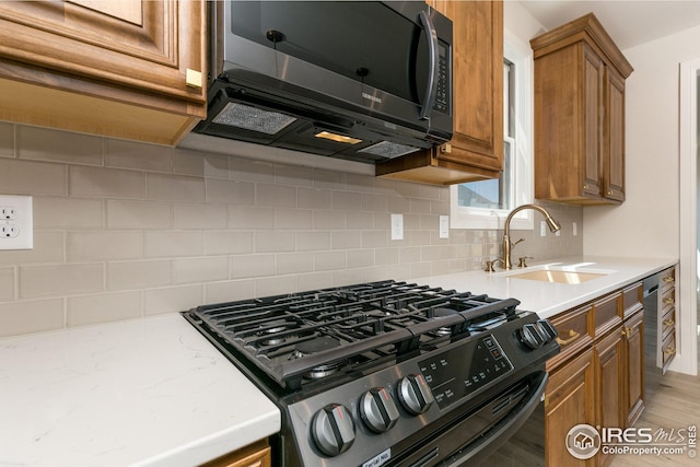 kitchen featuring tasteful backsplash, brown cabinetry, range with gas stovetop, light wood-type flooring, and a sink