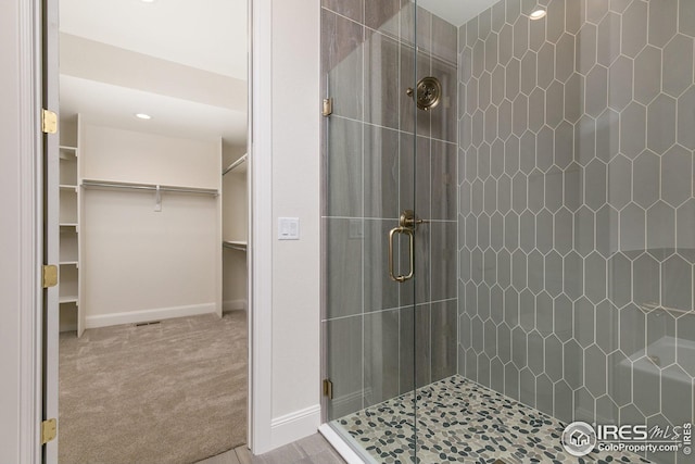 full bathroom with a shower stall, a walk in closet, and baseboards