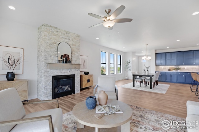 living room featuring recessed lighting, a stone fireplace, light wood-type flooring, baseboards, and ceiling fan with notable chandelier