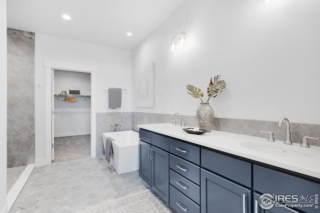 bathroom featuring tile walls, a sink, a spacious closet, and a freestanding bath