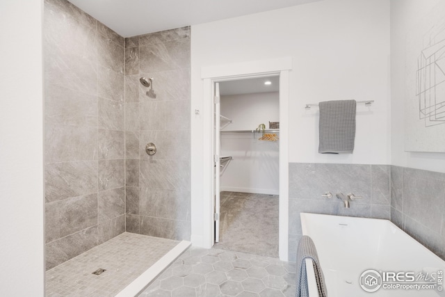 full bath with a walk in closet, tile walls, a freestanding bath, a tile shower, and tile patterned floors