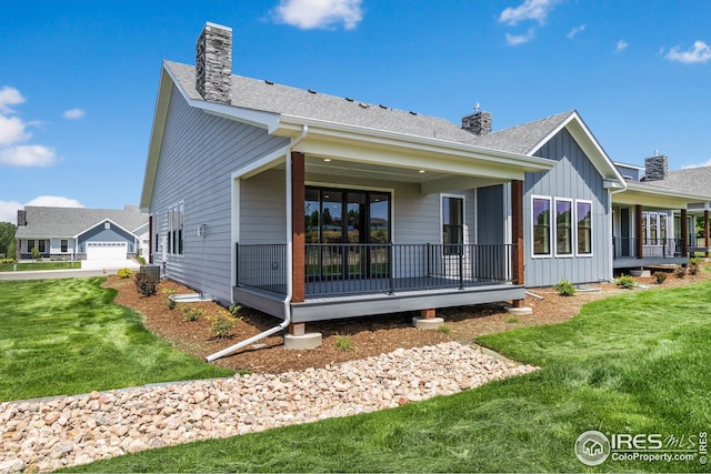 rear view of house featuring a yard, a chimney, a shingled roof, covered porch, and board and batten siding