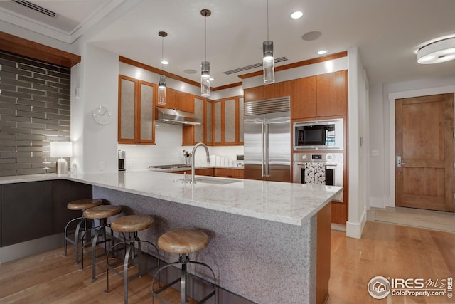 kitchen with kitchen peninsula, sink, built in appliances, and backsplash