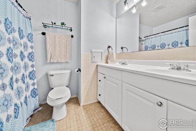 bathroom with tile patterned flooring, a textured ceiling, toilet, vanity, and tile walls