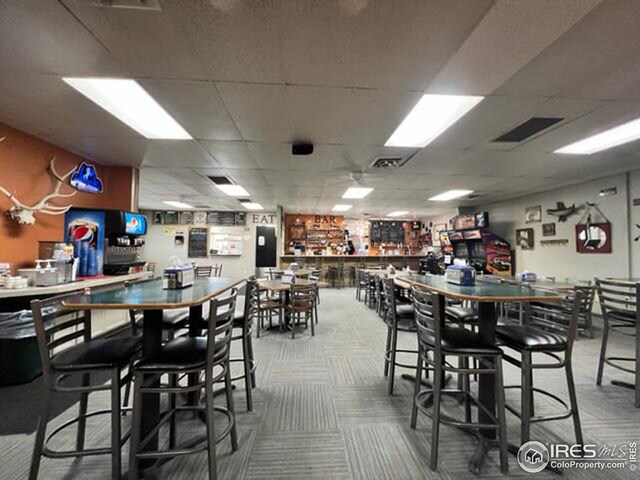 carpeted dining space with a paneled ceiling and bar area