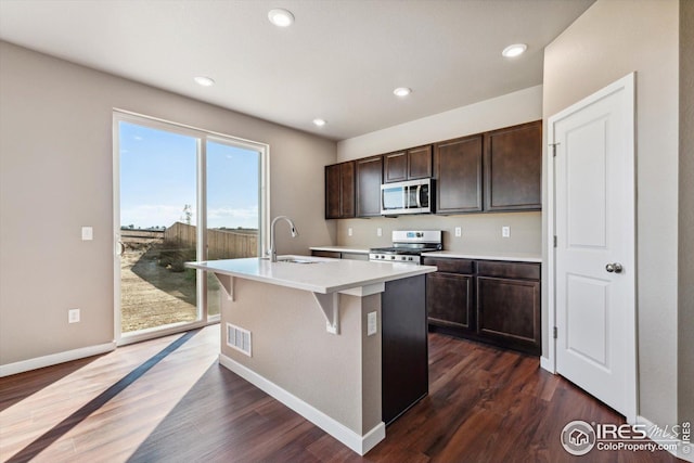 kitchen with sink, a kitchen breakfast bar, dark hardwood / wood-style flooring, a kitchen island with sink, and appliances with stainless steel finishes