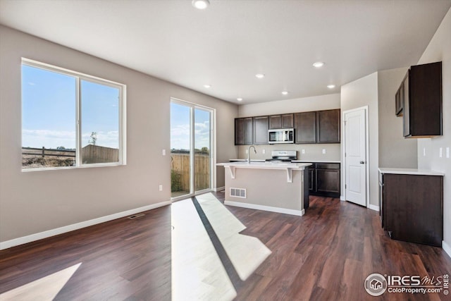 kitchen with dark brown cabinetry, range, an island with sink, and dark wood-type flooring