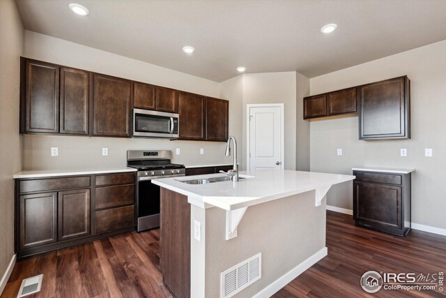 kitchen with dark brown cabinetry, sink, stainless steel appliances, dark hardwood / wood-style floors, and a kitchen island with sink