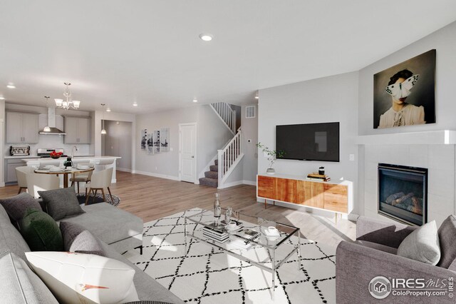 living room featuring an inviting chandelier, a tiled fireplace, and light hardwood / wood-style flooring