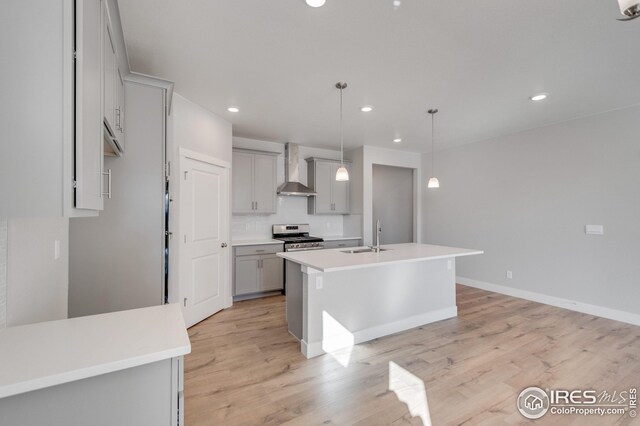 kitchen featuring gray cabinetry, stainless steel range, wall chimney exhaust hood, light hardwood / wood-style floors, and a kitchen island with sink