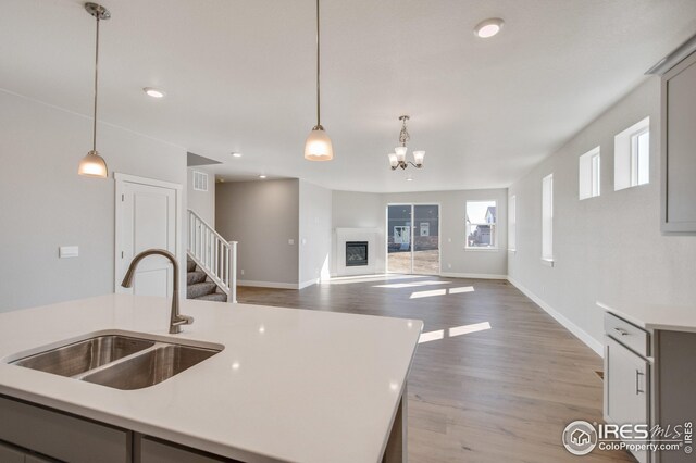 kitchen featuring sink, gray cabinets, light hardwood / wood-style floors, hanging light fixtures, and an island with sink