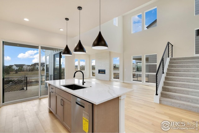 kitchen featuring a sink, hanging light fixtures, light wood-style floors, stainless steel dishwasher, and open floor plan