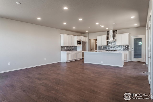 6105 Saddle Horn Dr, Timnath, CO 80547 - kitchen with wall chimney range hood, stainless steel microwave, tasteful backsplash, a kitchen island with sink, and recessed lighting