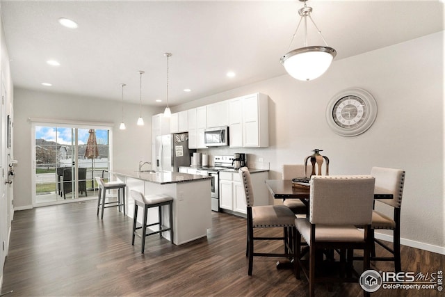 kitchen featuring appliances with stainless steel finishes, dark hardwood / wood-style flooring, a center island with sink, and decorative light fixtures