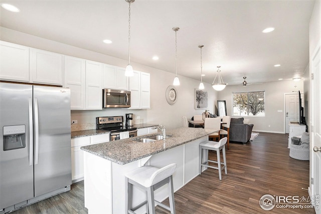 kitchen with light stone countertops, appliances with stainless steel finishes, dark hardwood / wood-style flooring, a center island with sink, and white cabinets