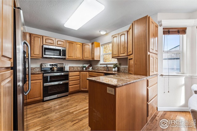 kitchen with kitchen peninsula, dark stone countertops, light wood-type flooring, and appliances with stainless steel finishes